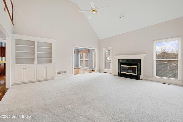 unfurnished living room with high vaulted ceiling, carpet flooring, a ceiling fan, visible vents, and a high end fireplace