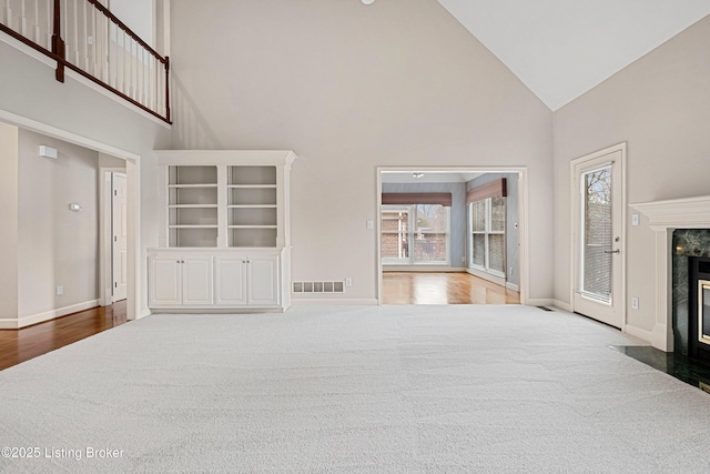 unfurnished living room with high vaulted ceiling, a premium fireplace, carpet flooring, and baseboards