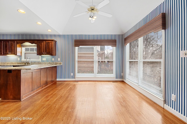 kitchen featuring light wood-style floors, light stone countertops, vaulted ceiling, and a ceiling fan