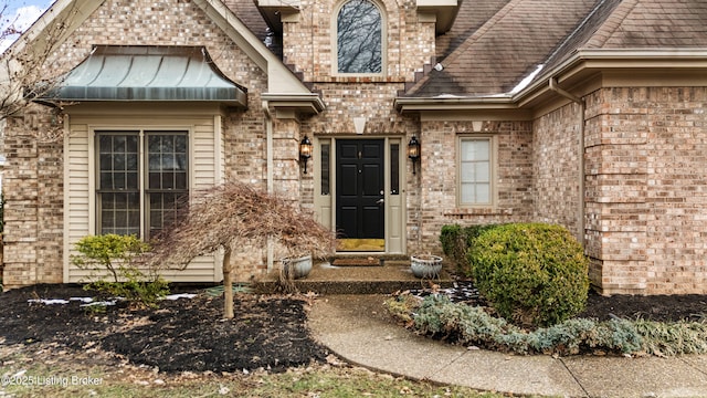 view of exterior entry featuring a shingled roof and brick siding