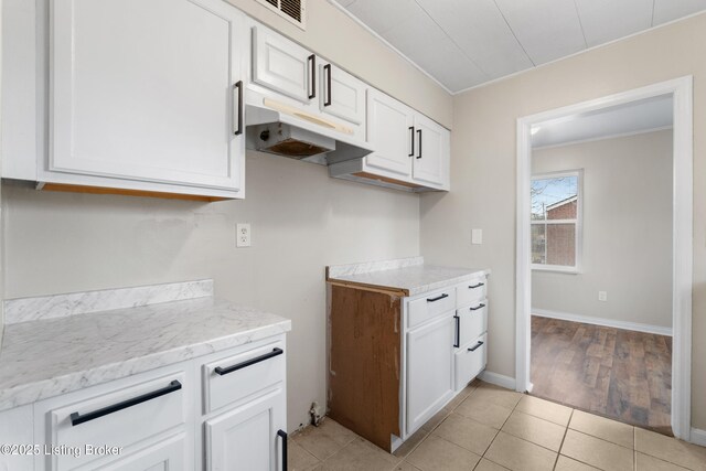 kitchen with light stone countertops, under cabinet range hood, ornamental molding, light tile patterned floors, and white cabinetry