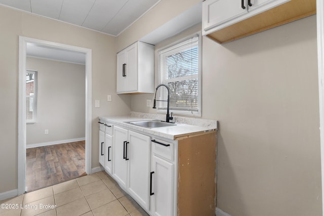 kitchen with a sink, light tile patterned flooring, white cabinets, light countertops, and baseboards