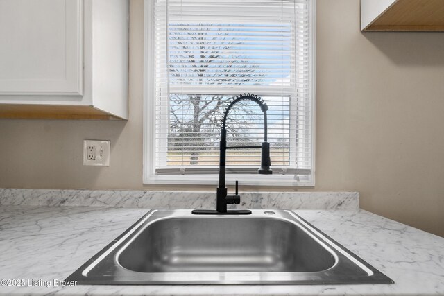 kitchen featuring white cabinetry, light stone counters, and a sink