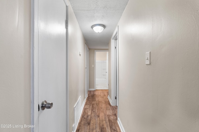 hallway featuring visible vents, baseboards, a textured ceiling, and wood finished floors