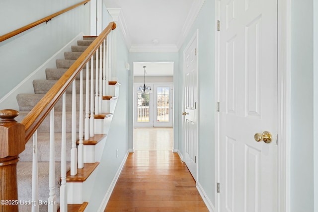 interior space with crown molding, light wood finished floors, a chandelier, baseboards, and stairs