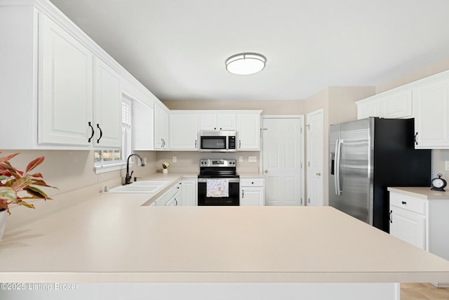 kitchen featuring stainless steel appliances, light countertops, a sink, and a peninsula