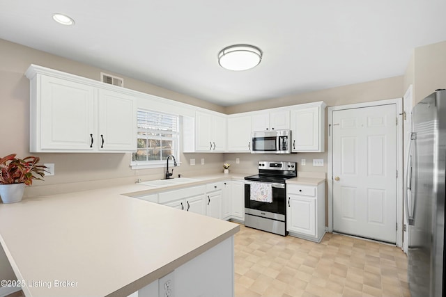 kitchen featuring visible vents, white cabinets, appliances with stainless steel finishes, a peninsula, and a sink