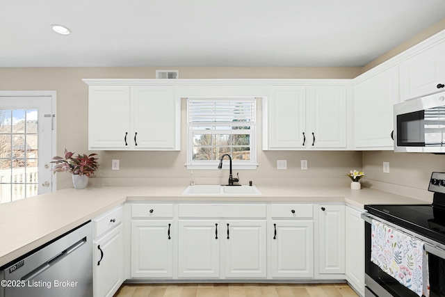 kitchen with a sink, visible vents, white cabinets, light countertops, and appliances with stainless steel finishes