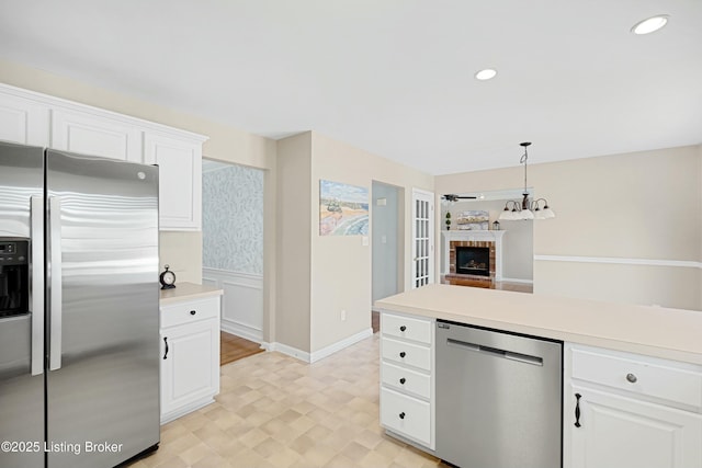 kitchen with decorative light fixtures, a fireplace, stainless steel appliances, light countertops, and white cabinets