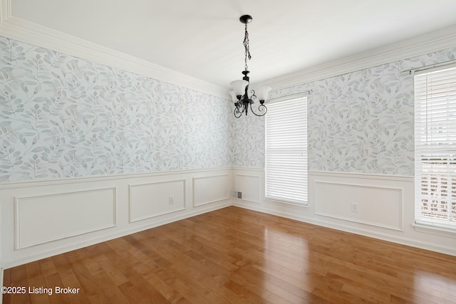 unfurnished dining area with hardwood / wood-style flooring, wallpapered walls, a chandelier, and a wainscoted wall