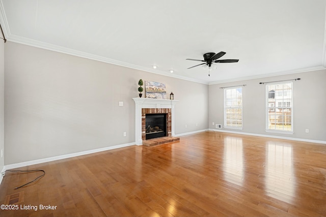 unfurnished living room featuring light wood finished floors, ornamental molding, a ceiling fan, a brick fireplace, and baseboards