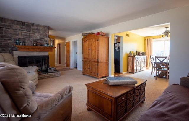 living room with a large fireplace, ceiling fan, and light carpet