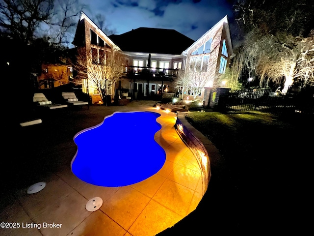 pool at night featuring a patio area, a fenced in pool, and fence