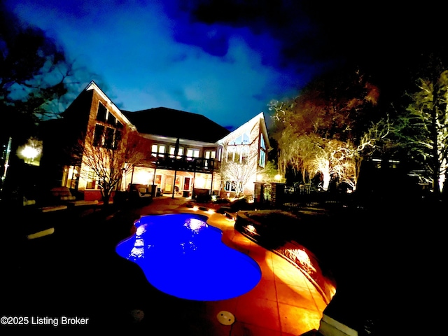 back of house at night featuring a patio and an outdoor pool