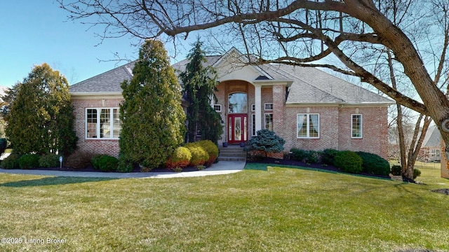 view of front of home featuring brick siding, a chimney, a front lawn, and roof with shingles