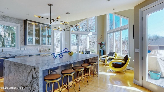 kitchen featuring a spacious island, an inviting chandelier, light wood finished floors, glass insert cabinets, and light stone countertops