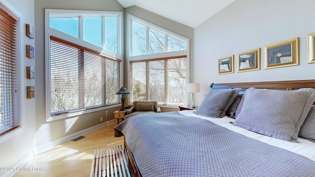 bedroom with visible vents, high vaulted ceiling, baseboards, and wood finished floors