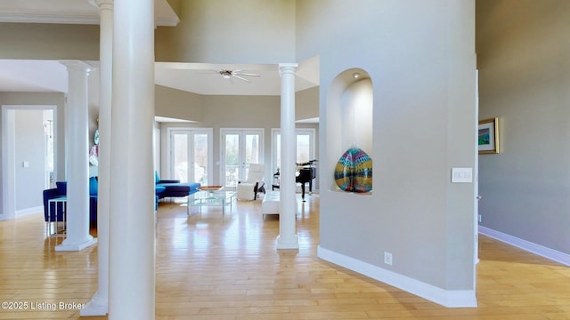 hallway with light wood-style floors, decorative columns, baseboards, and a high ceiling