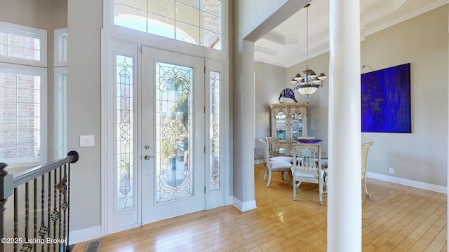 entrance foyer featuring an inviting chandelier, light wood-style flooring, crown molding, and a healthy amount of sunlight