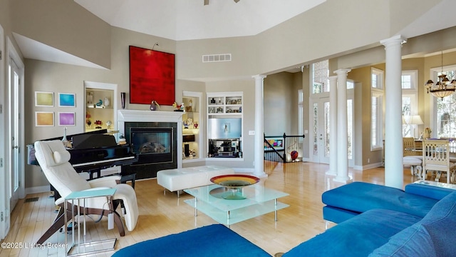 living area featuring built in features, wood finished floors, visible vents, ornate columns, and a high ceiling