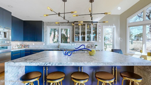 kitchen with blue cabinetry, a breakfast bar area, light countertops, stainless steel oven, and a warming drawer