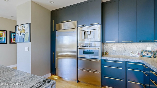 kitchen with a warming drawer, light wood-style flooring, blue cabinetry, appliances with stainless steel finishes, and decorative backsplash