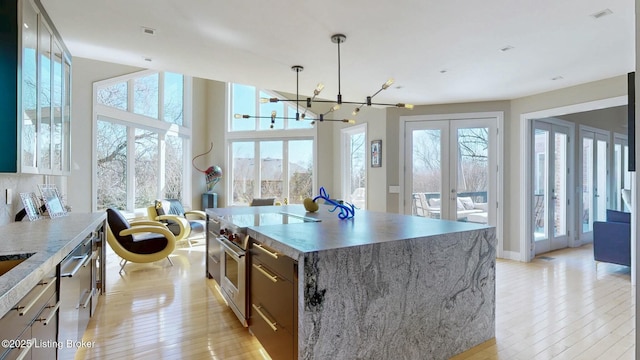 kitchen with high end stove, hanging light fixtures, french doors, light wood-style floors, and a center island