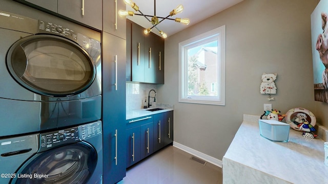 laundry area featuring visible vents, baseboards, a sink, stacked washer / dryer, and a notable chandelier