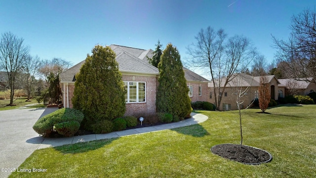 view of side of property featuring a yard, brick siding, and driveway