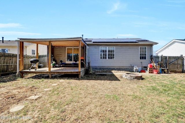 rear view of house featuring a deck, a fenced backyard, a yard, a fire pit, and solar panels