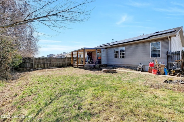 exterior space with roof mounted solar panels, a lawn, a fenced backyard, and an outdoor fire pit