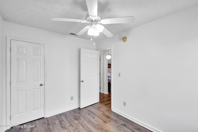 unfurnished bedroom featuring wood finished floors, visible vents, baseboards, ceiling fan, and a textured ceiling