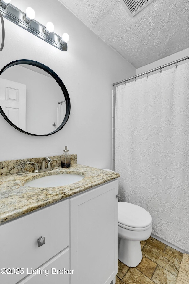 bathroom featuring vanity, a textured ceiling, visible vents, stone finish flooring, and toilet