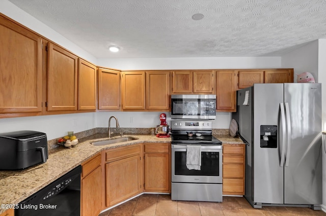 kitchen featuring light stone countertops, a sink, appliances with stainless steel finishes, a textured ceiling, and brown cabinets