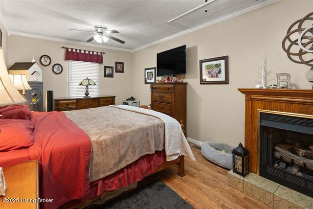 bedroom with a fireplace with raised hearth, ornamental molding, wood finished floors, and attic access