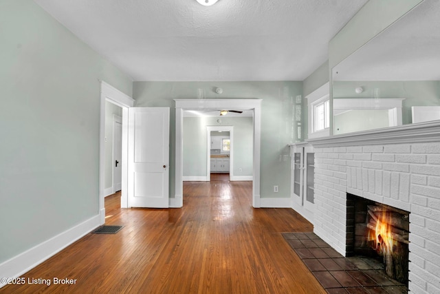 unfurnished living room with visible vents, baseboards, a brick fireplace, and wood finished floors