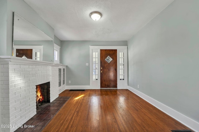 foyer entrance with a fireplace, a textured ceiling, baseboards, and wood finished floors