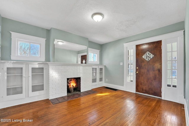 foyer entrance featuring visible vents, a brick fireplace, baseboards, hardwood / wood-style flooring, and a textured ceiling