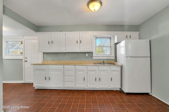 kitchen featuring a wealth of natural light, light countertops, freestanding refrigerator, and a sink