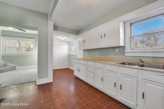 kitchen featuring white cabinetry, light countertops, baseboards, and a sink