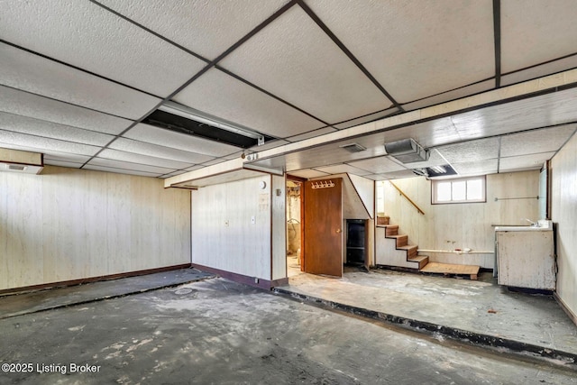 basement with a drop ceiling, stairway, and wooden walls