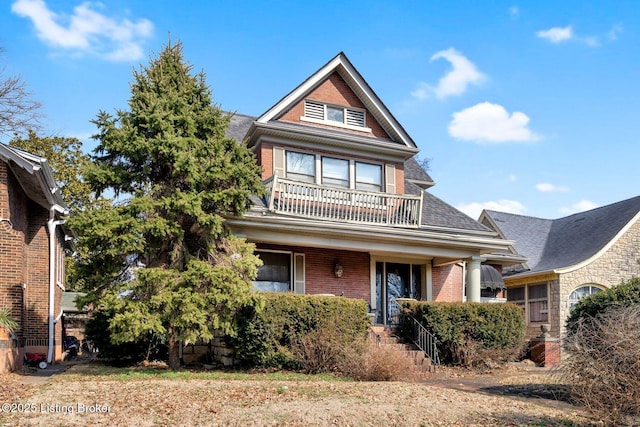 view of front of home with a shingled roof, brick siding, and a balcony