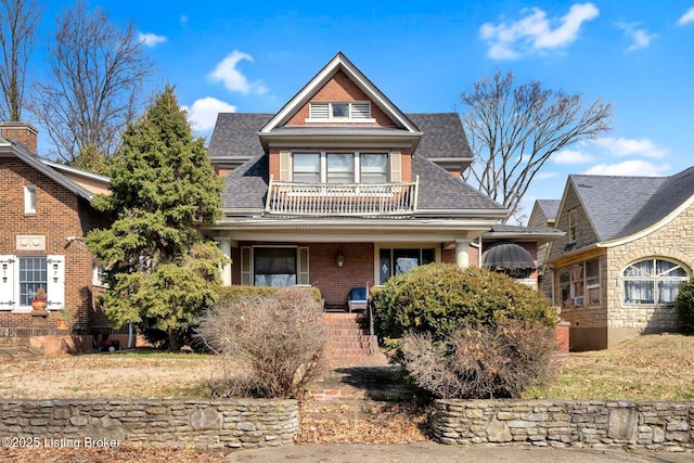 view of front of home featuring a shingled roof, brick siding, and a balcony