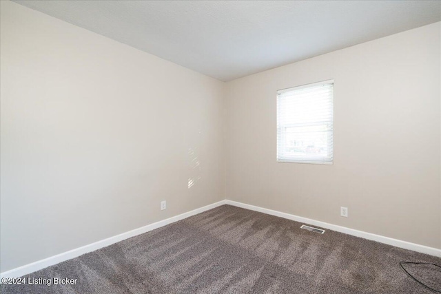 unfurnished room featuring dark colored carpet, visible vents, and baseboards