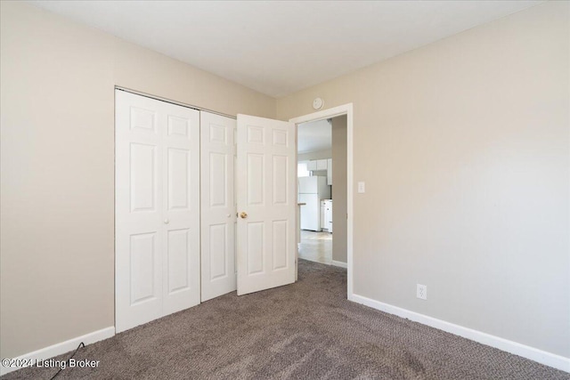 unfurnished bedroom featuring carpet floors, freestanding refrigerator, a closet, and baseboards