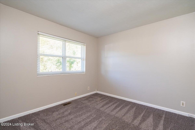 spare room with visible vents, dark carpet, and baseboards