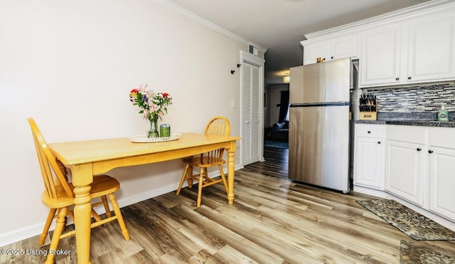 kitchen featuring white cabinetry, light wood-style floors, freestanding refrigerator, decorative backsplash, and crown molding