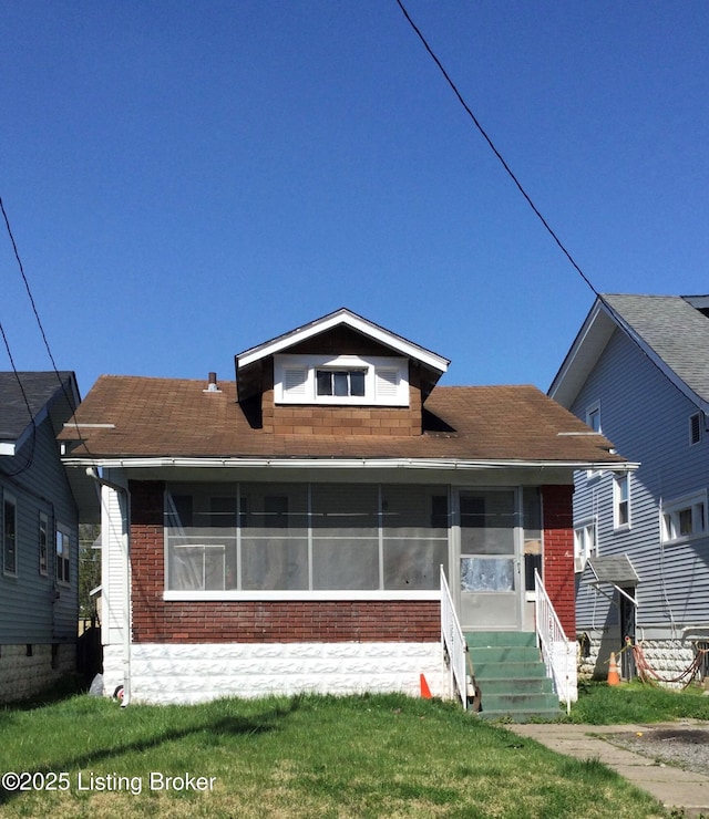 bungalow with entry steps, a sunroom, brick siding, and a front lawn