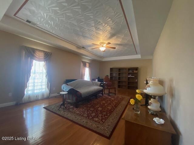 bedroom featuring multiple windows, baseboards, a raised ceiling, and wood finished floors