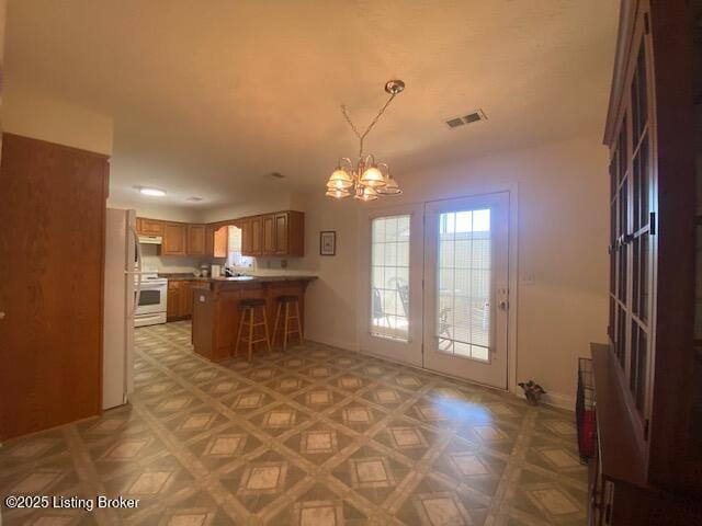 kitchen featuring a breakfast bar area, white appliances, visible vents, brown cabinets, and an inviting chandelier